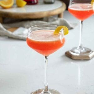 Aperol gin sour cocktail on table with lemon peel on rim.