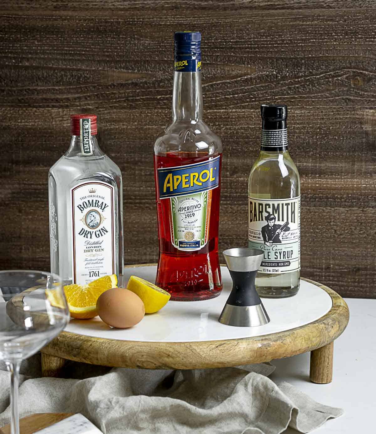 Gin, Aperol, simple syrup, lemon and an egg on table.