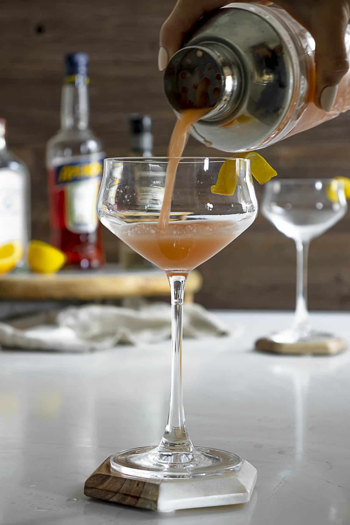 Pouring an Aperol sour with gin into a coupe glass.