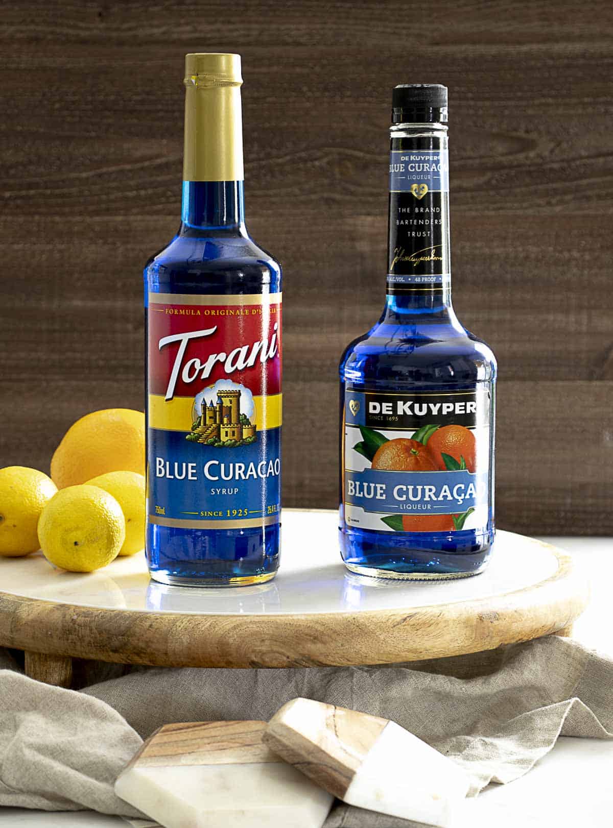 Bottle of blue curacao syrup and blue curacao liqueur next to one another.