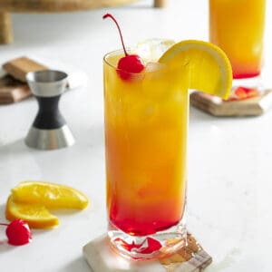 Vodka sunrise cocktail on table with cherry and orange slice.