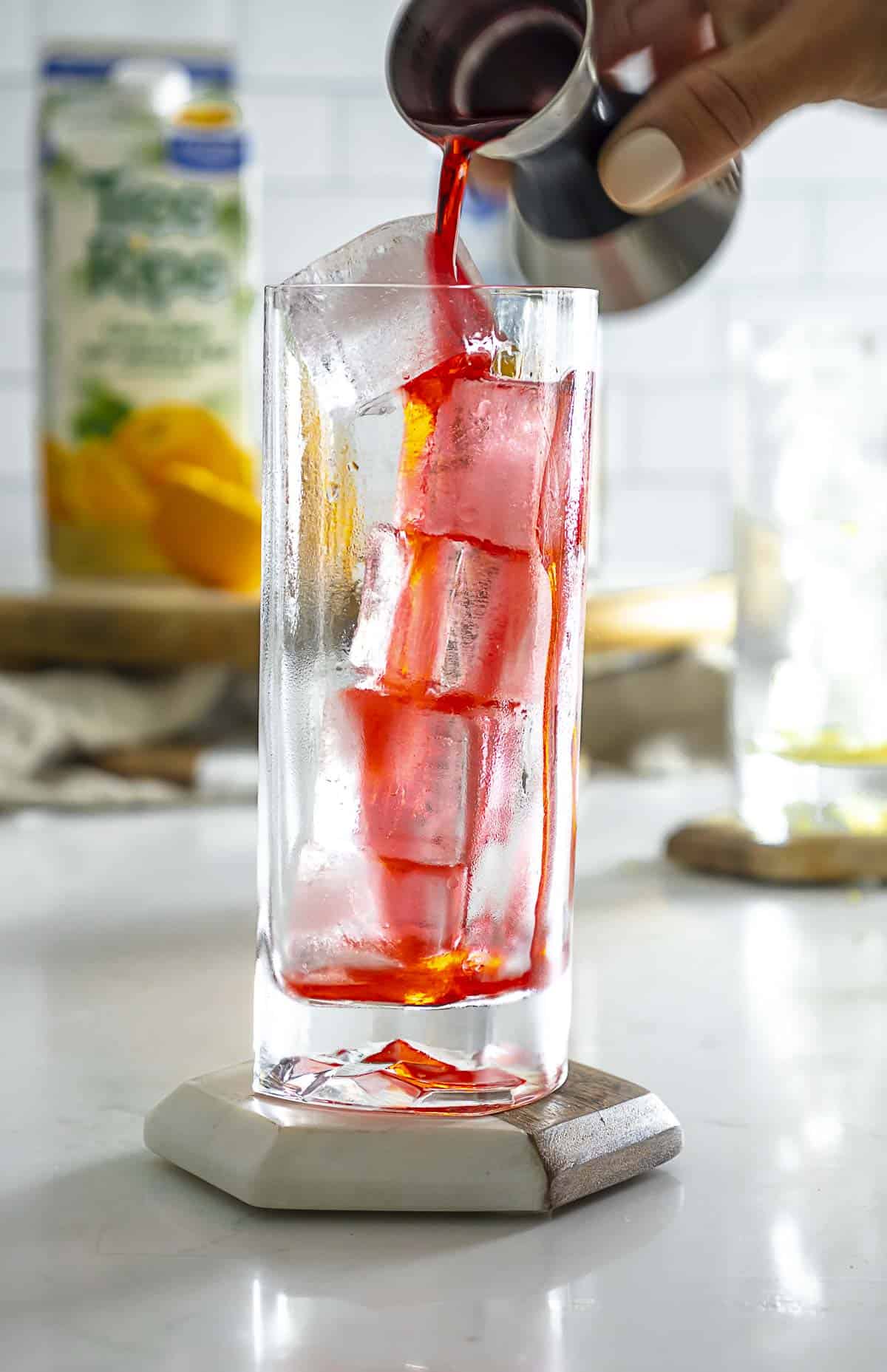 Pouring grenadine syrup into tall highball glass with ice.