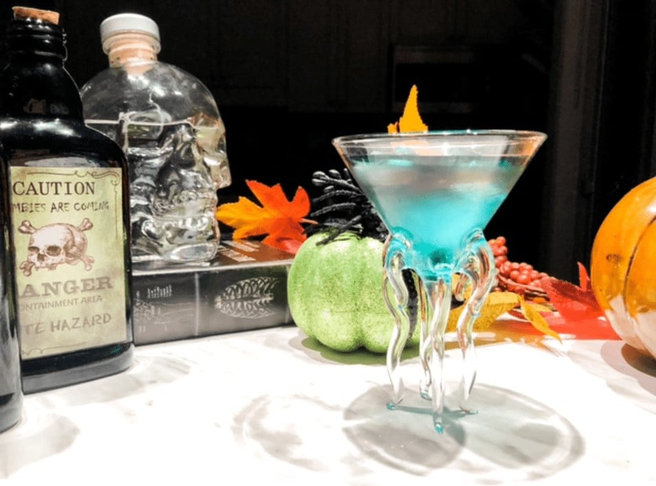 Blue coocktail on table with liquor bottles and fall decorations.