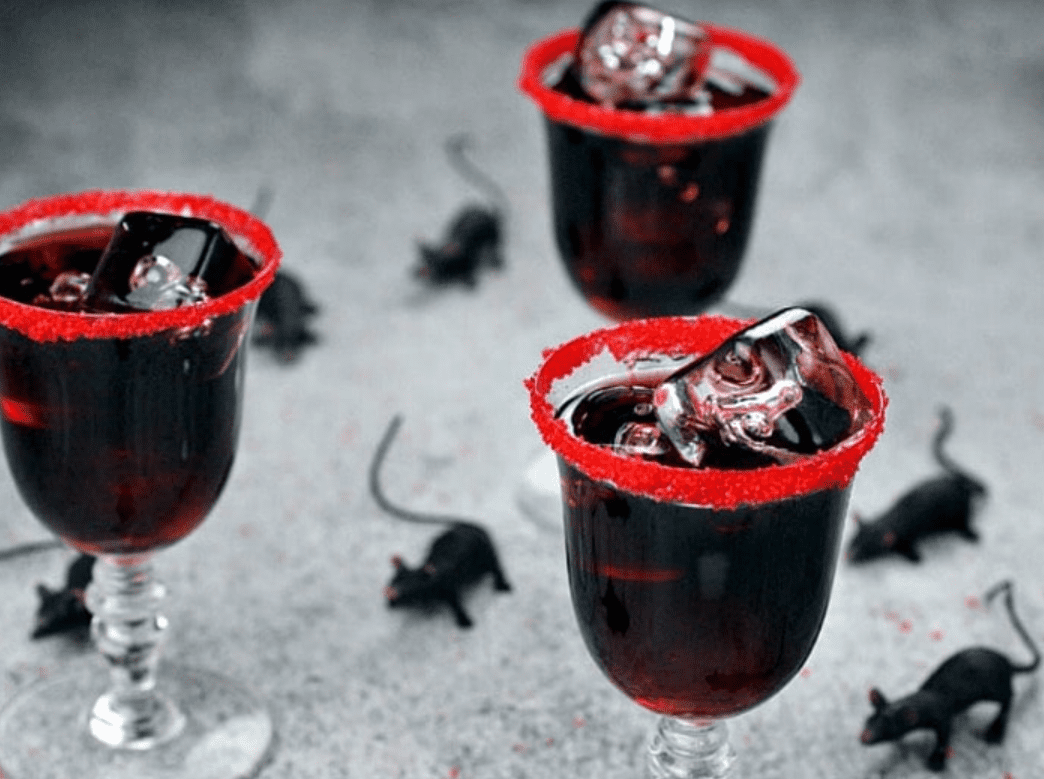 Black cocktails with red sugar rims with ice and halloween decorations. 