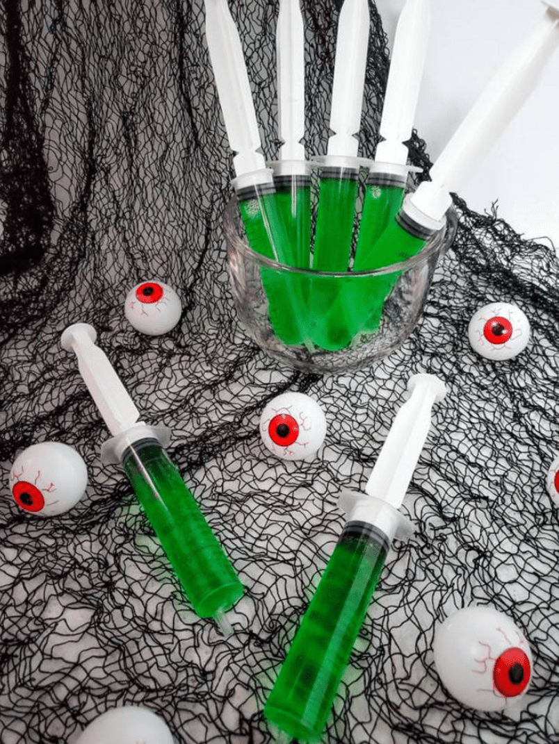 Green jello in syringes with halloween decorations. 