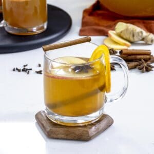 Hot mulled apple cider in clear mug with spiced and orange.