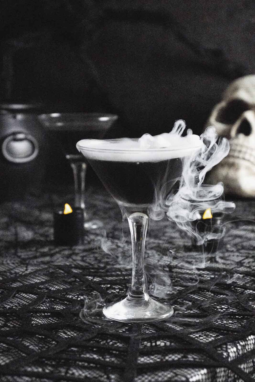 Black vodka martini with smoke on dark table.