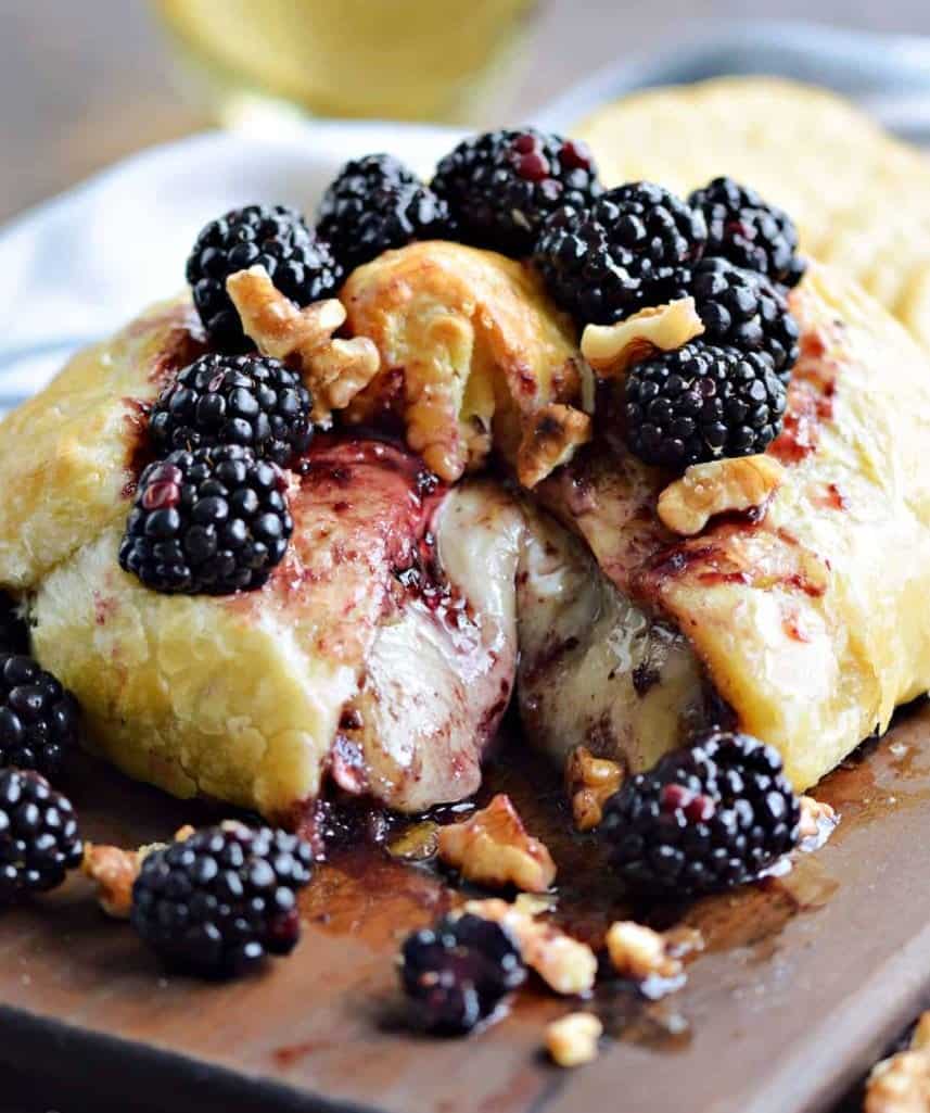 Baked brie with blackberries on a cutting board.