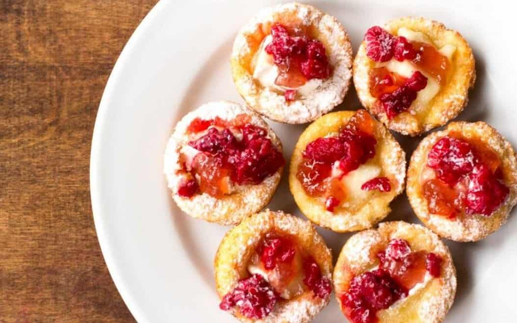 Brie bite cups with raspberry on a white plate on a counter.