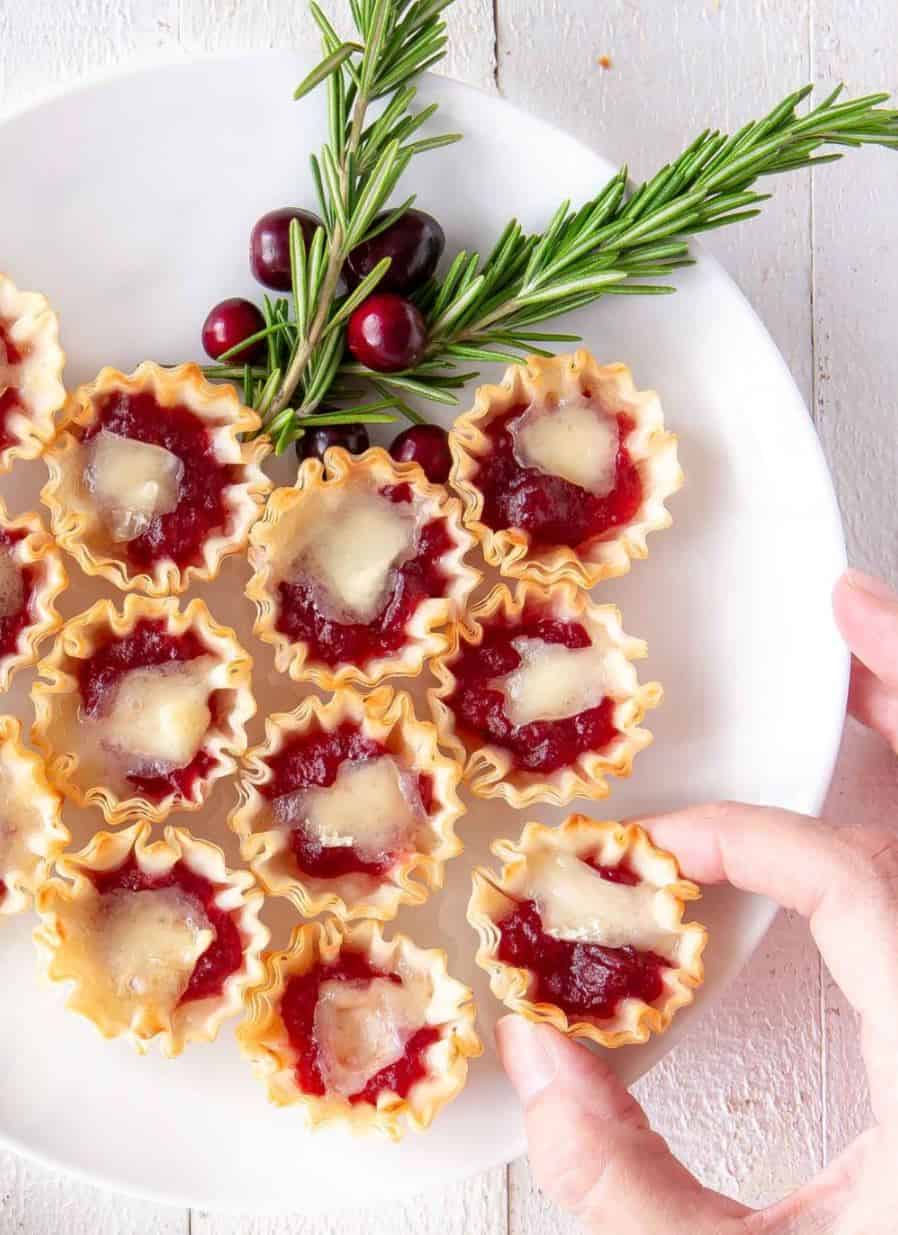 Cranberry orange brie cups with a sprig of rosemary on a white plate.  