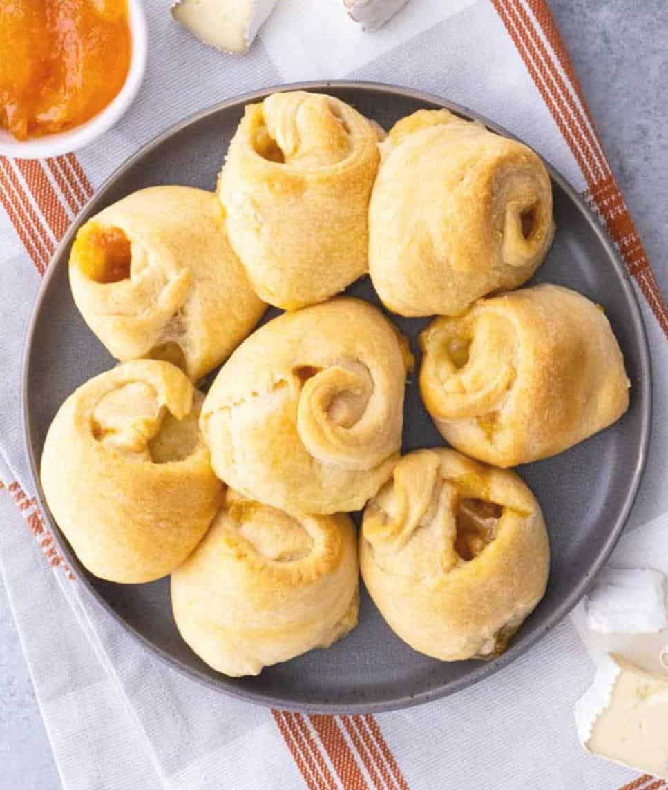 Brie knots on a grey plate with apricot jam in a dish. 