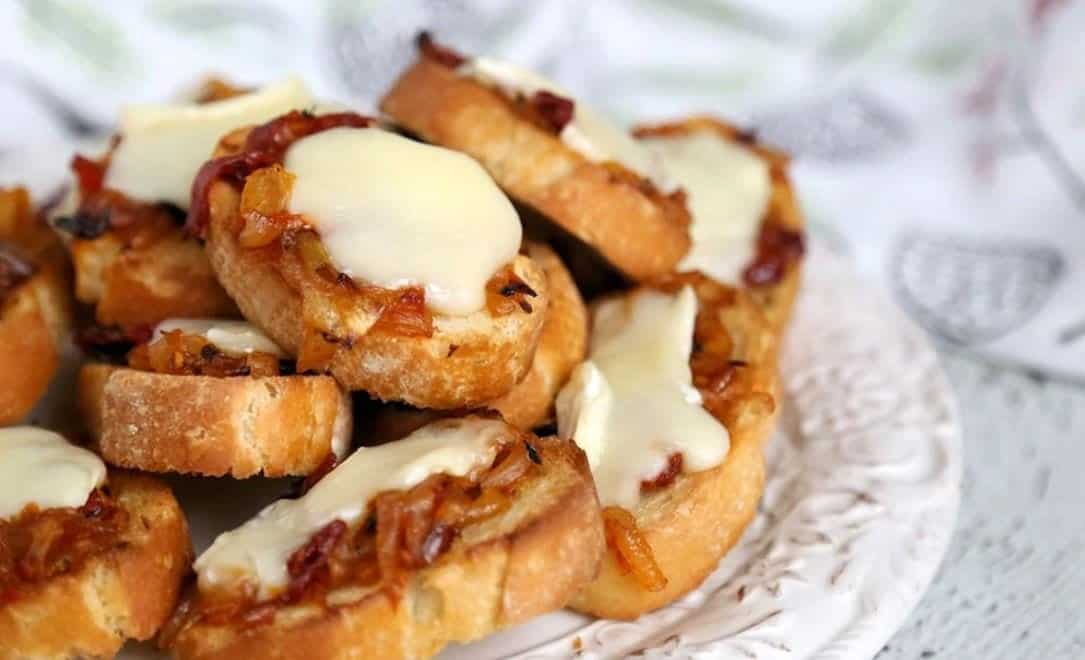 Crostinis with melted brie cheese on a white table.