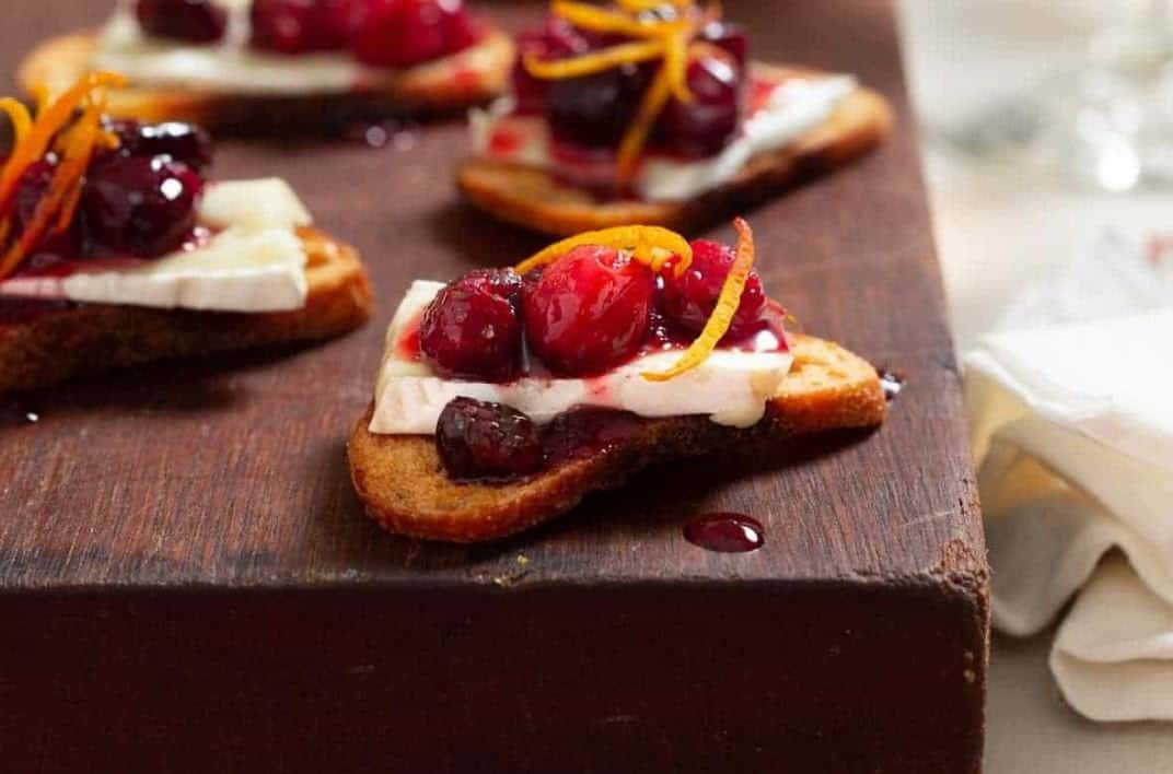 Cranberry and brie crostini on a wooden chopping block.