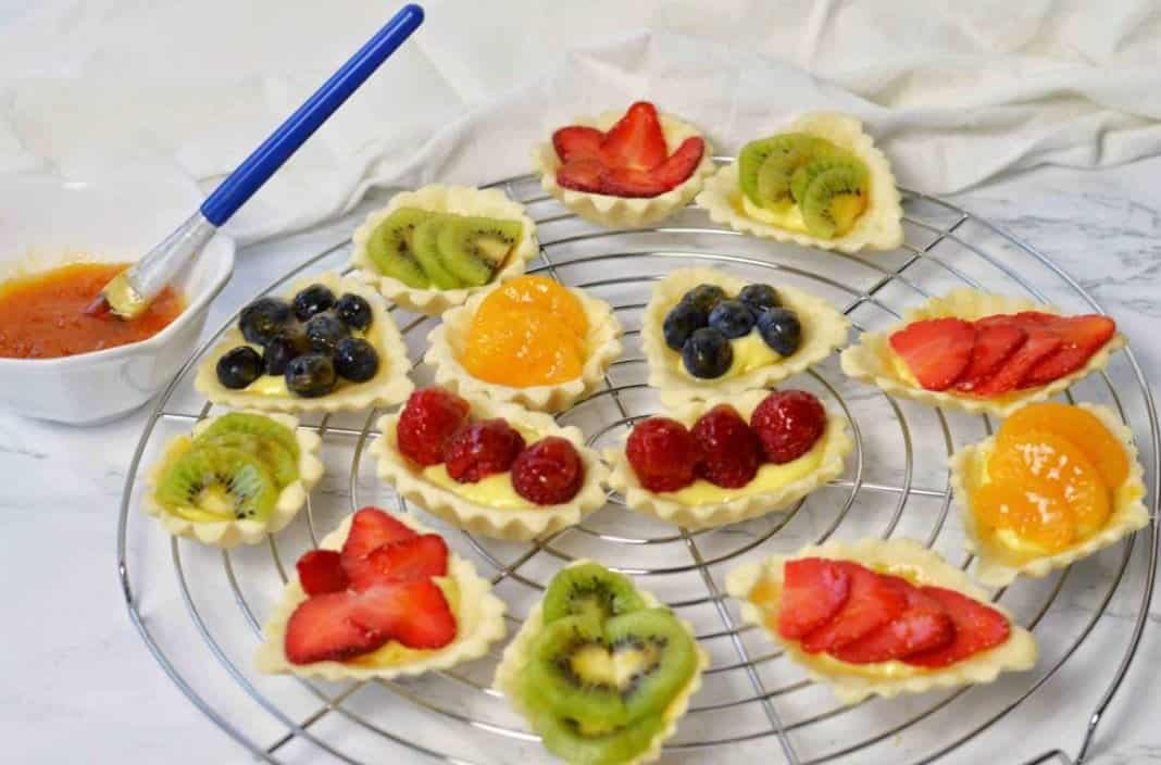 Fruit tarts on a cooling rack with a bowl of glaze. 