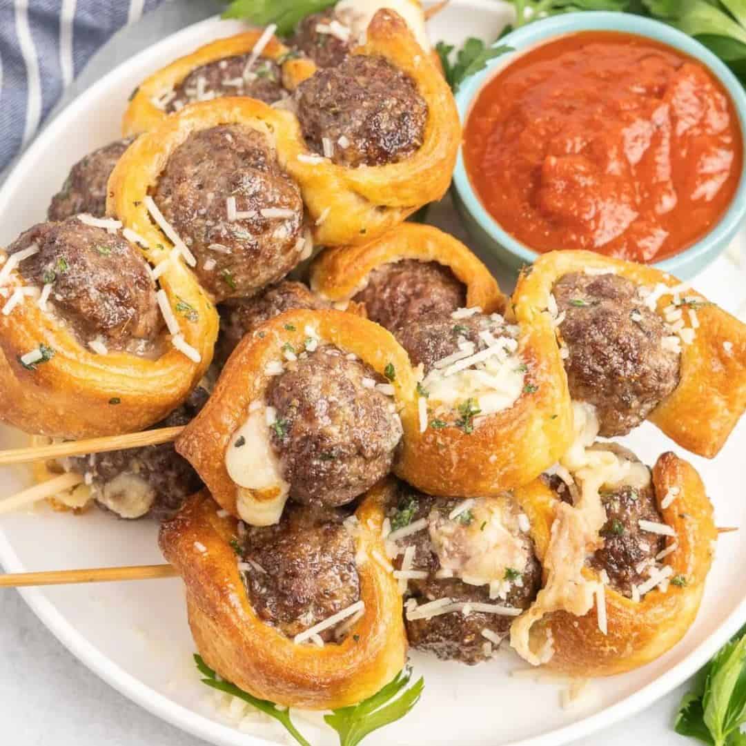 meatballs and puff pastry on a skewer with marinara sauce on the side.