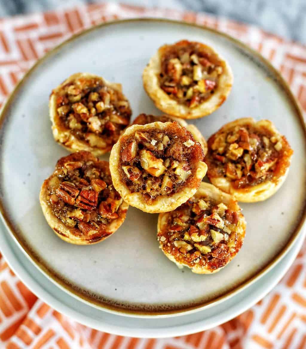 Mini pecan pies on a plate with patterned background. 