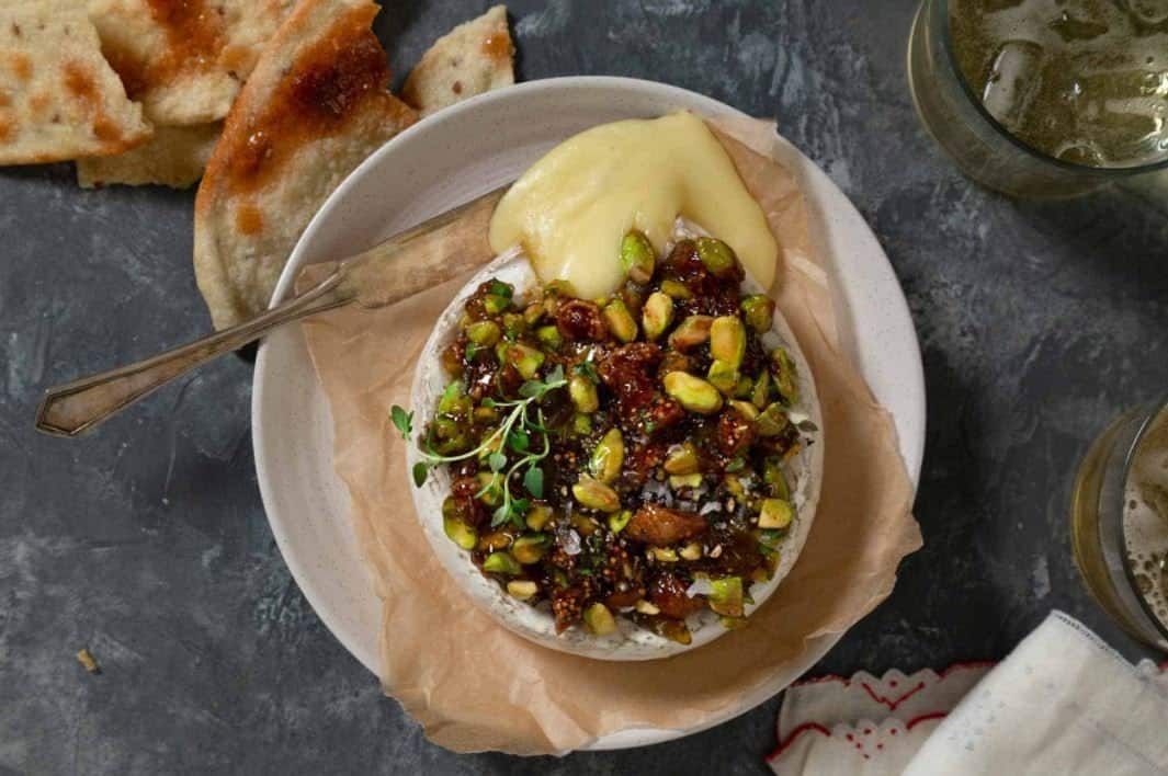 Baked brie with figs and pistachios on a white plate and black counter. 