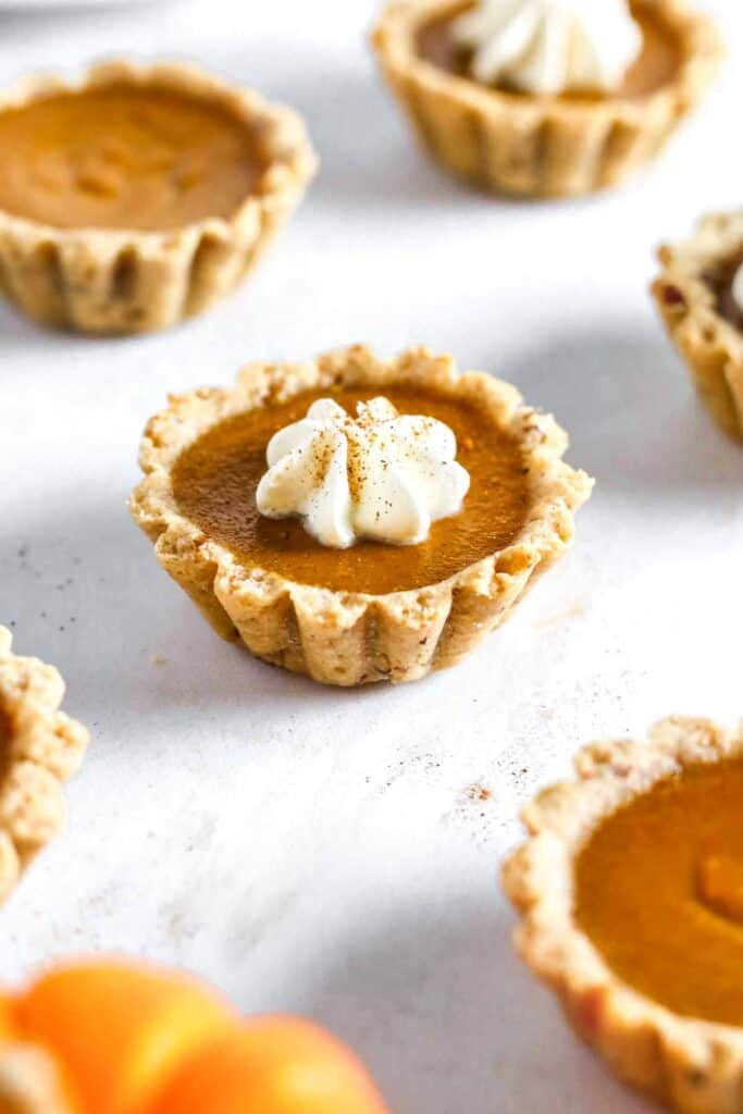 Mini pumpkin pie tartlets on table with whipped cream.