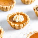 Mini pumpkin pie tartlets on table with wihipped cream.