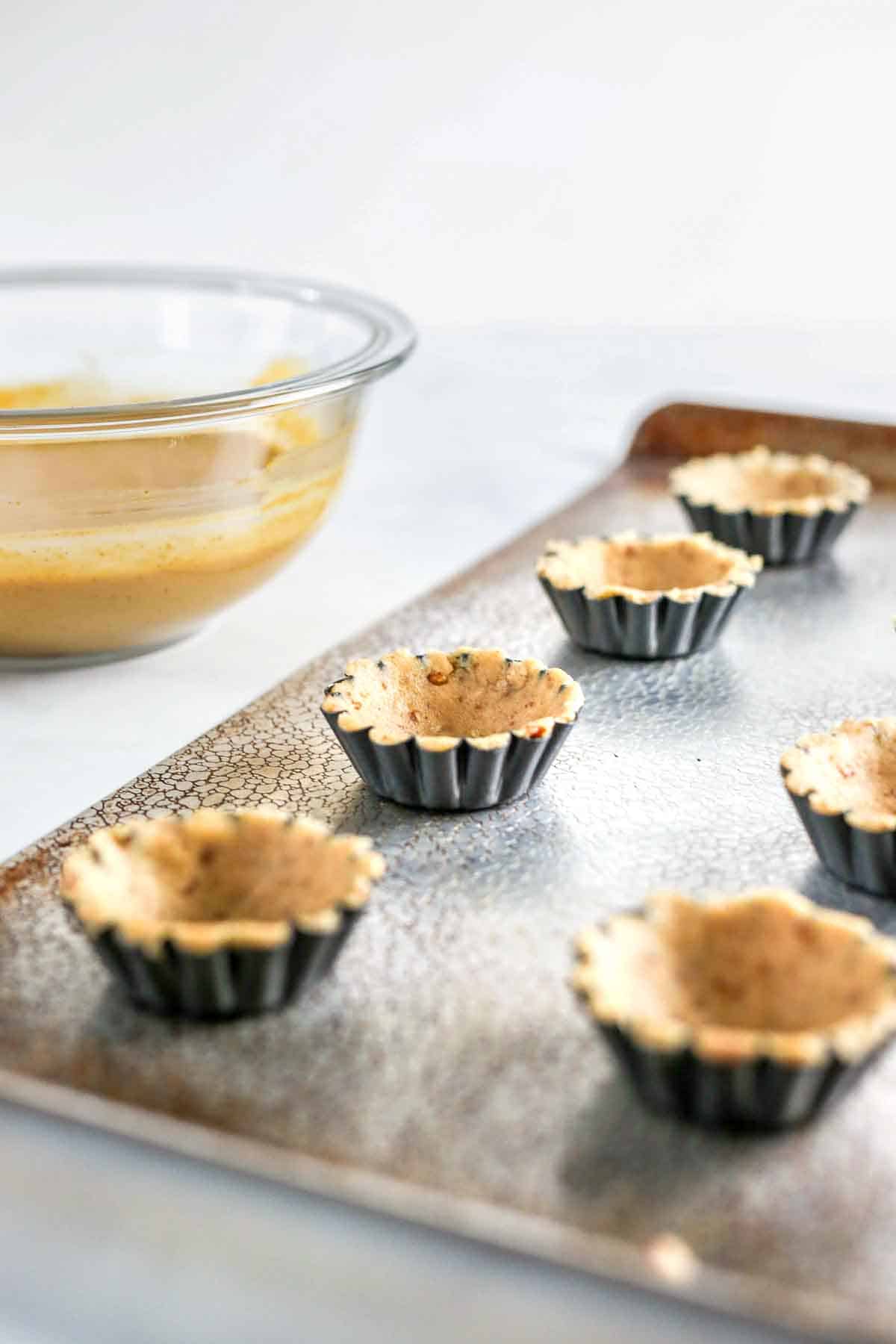 Pumpkin pie tartlets crust in mini tart shells on baking pan.