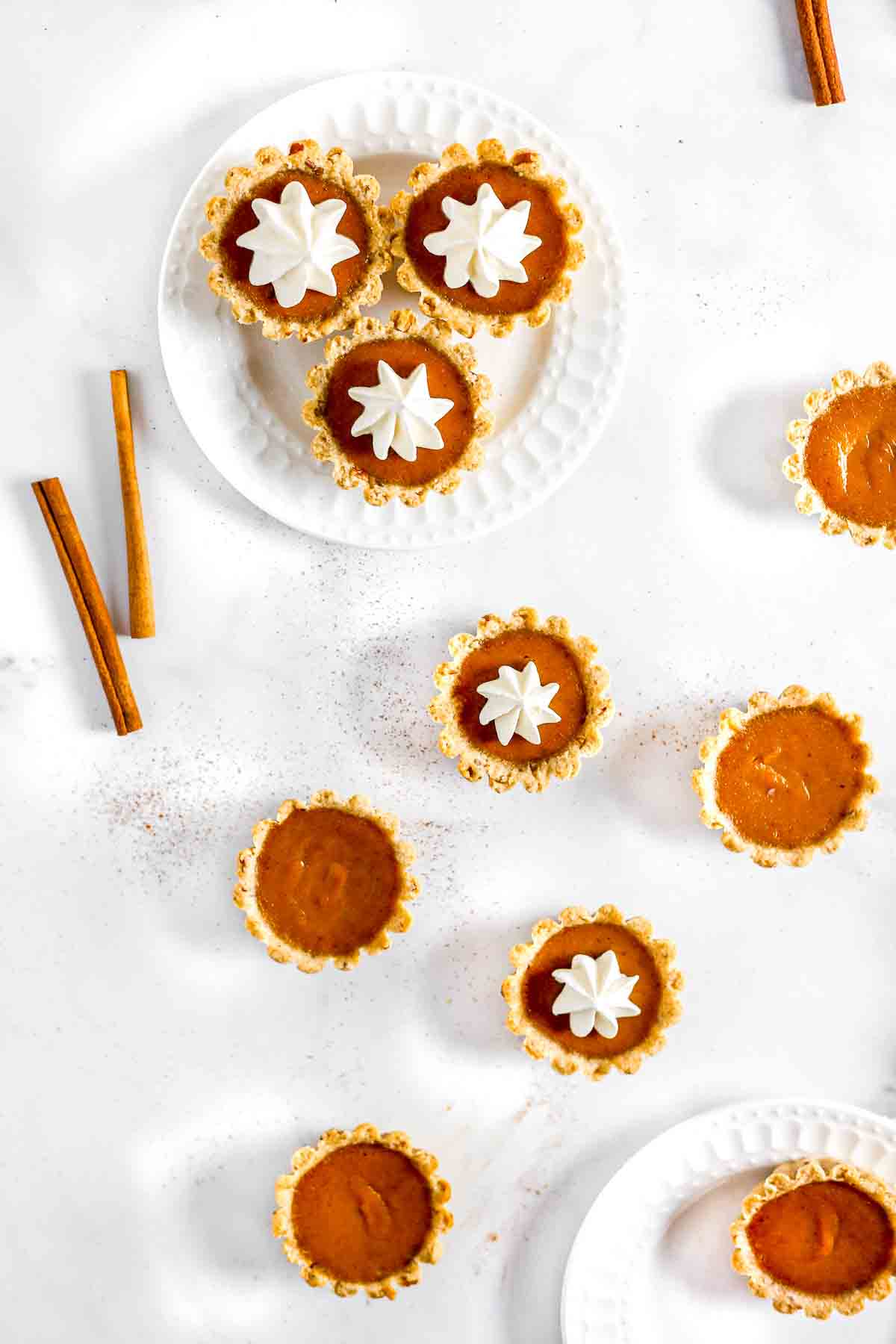 Mini pumpkin pies tarts on table with cinnamon and whipped cream.