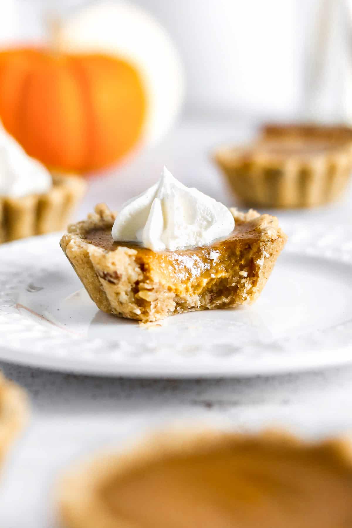 Pumpkin pie tartlet with a bite taken out of it on a plate.