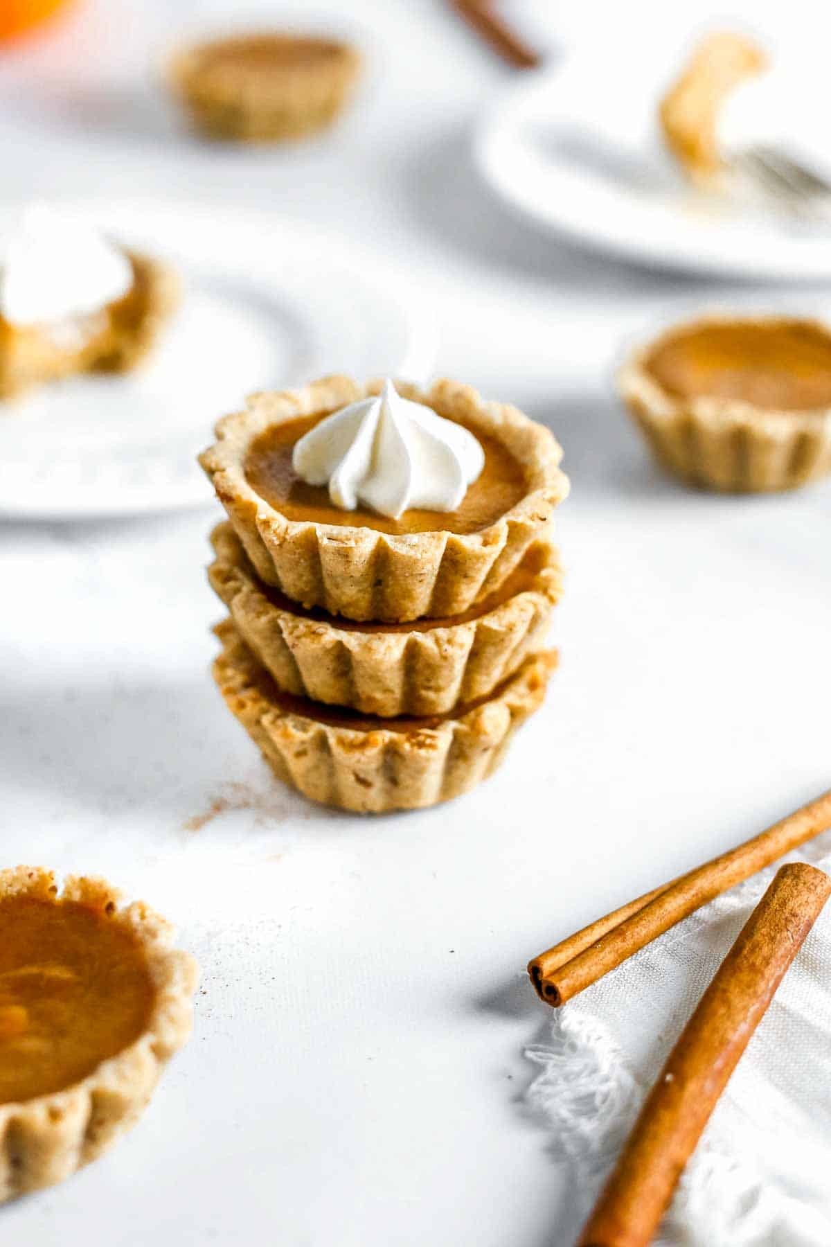 Pumpkin pie tartlets stacked on top of eachother with whipped cream.