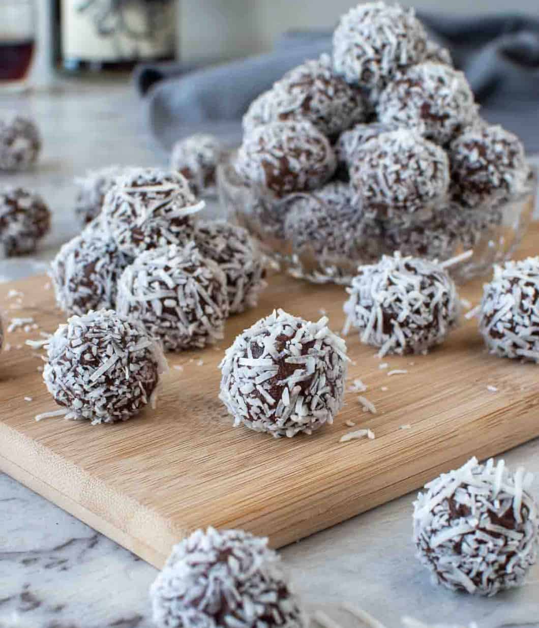 Truffle balls covered in coconut on a wooden cutting board.