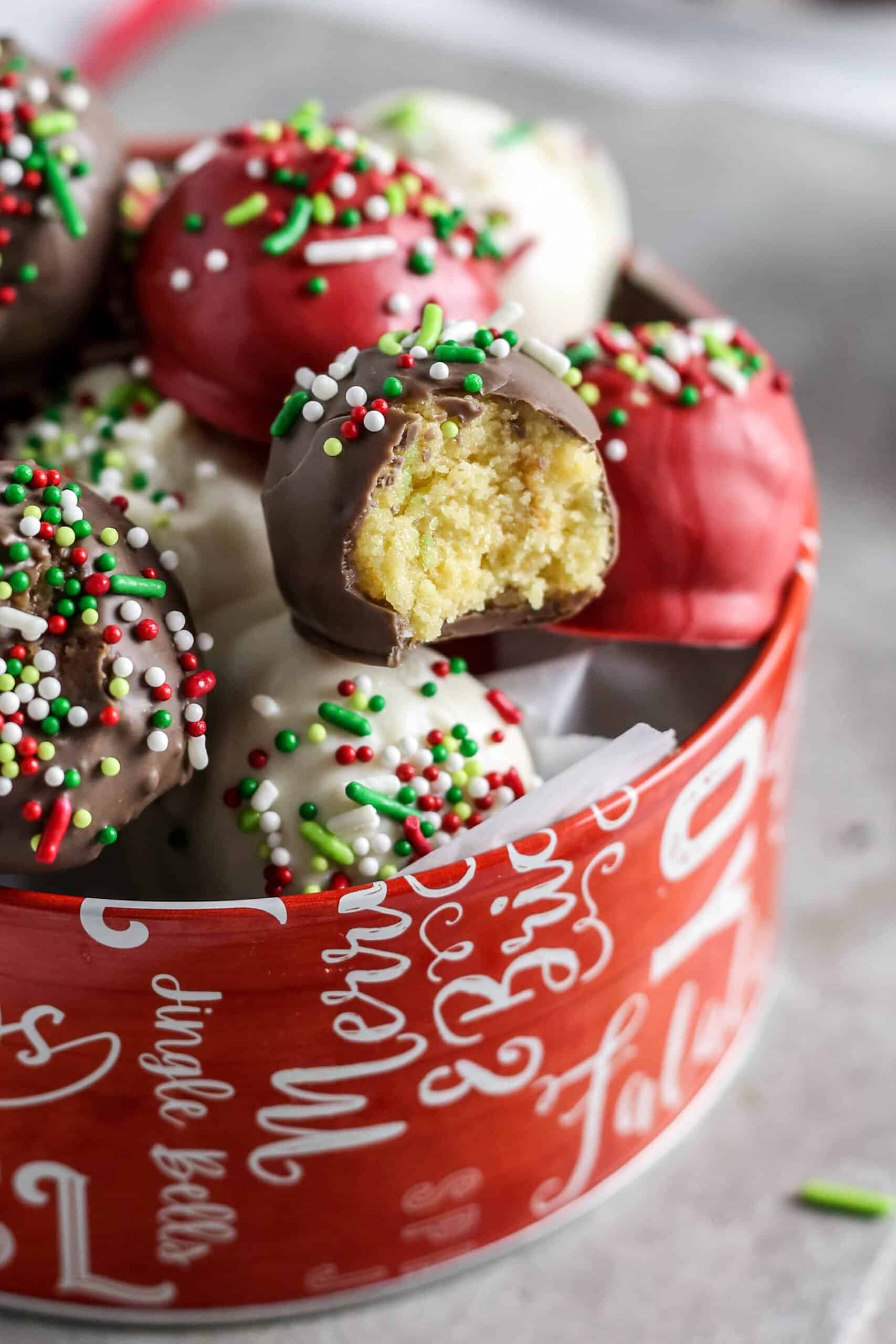 Christmas cake balls in holiday tins with sprinkles.