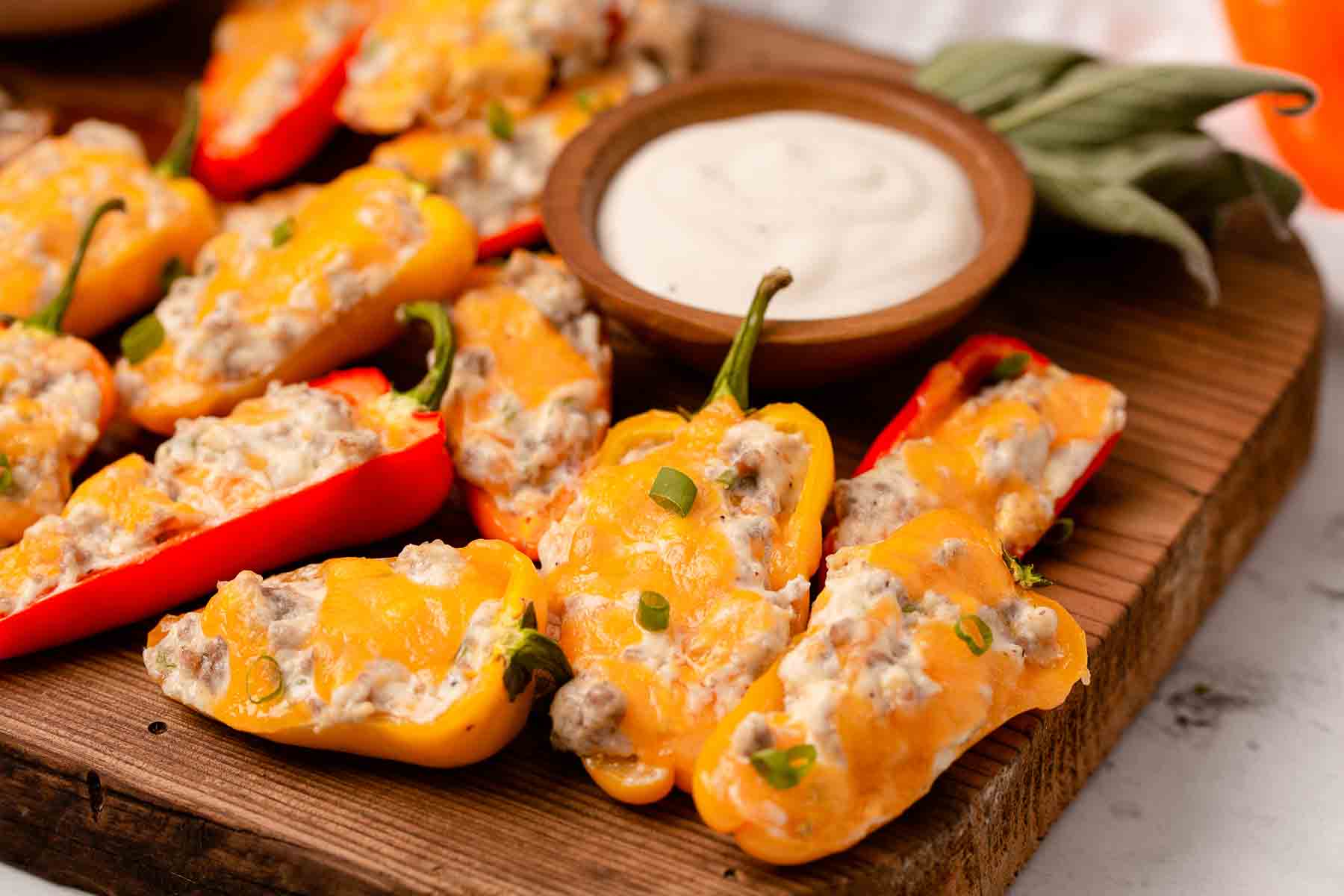 Sausage Stuffed Mini Bell Peppers With Cream Cheese on cutting board with dipping sauce.