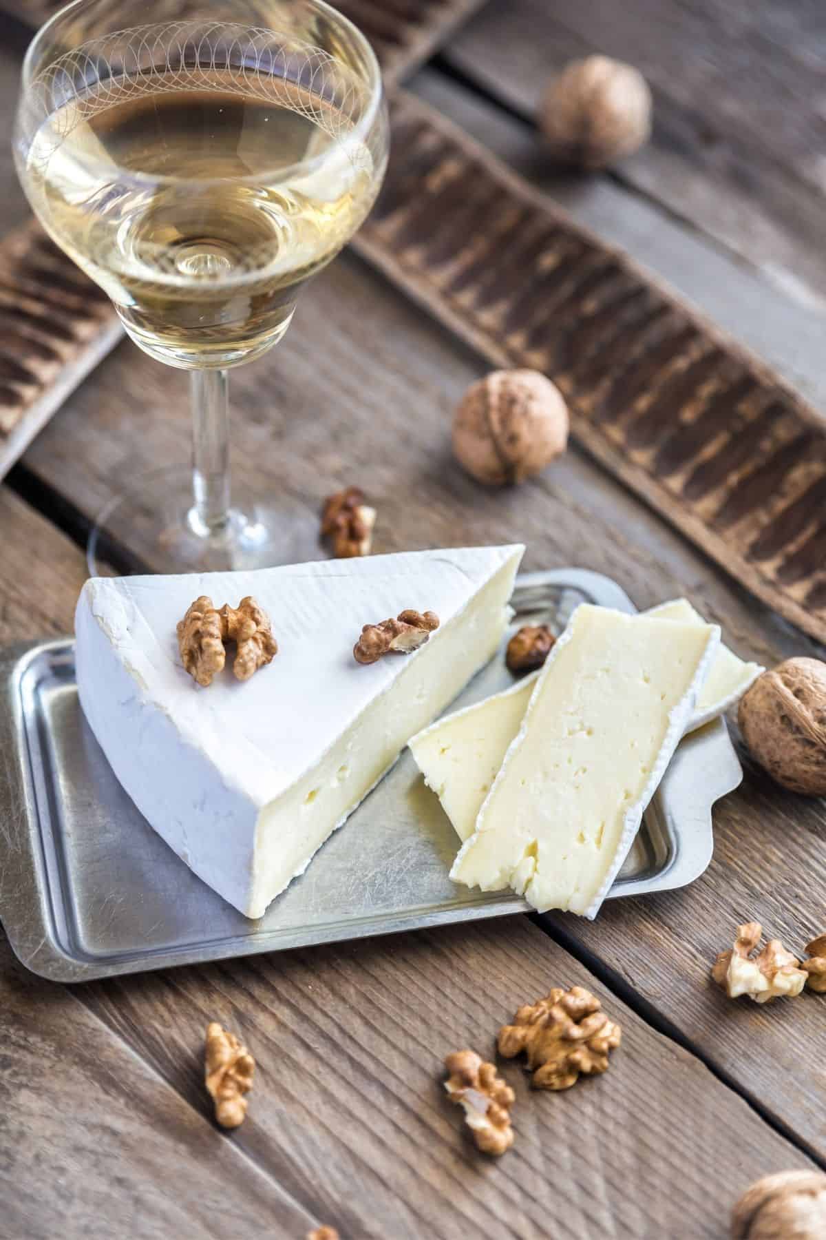 Brie cheese on cutting board with nuts and wine.