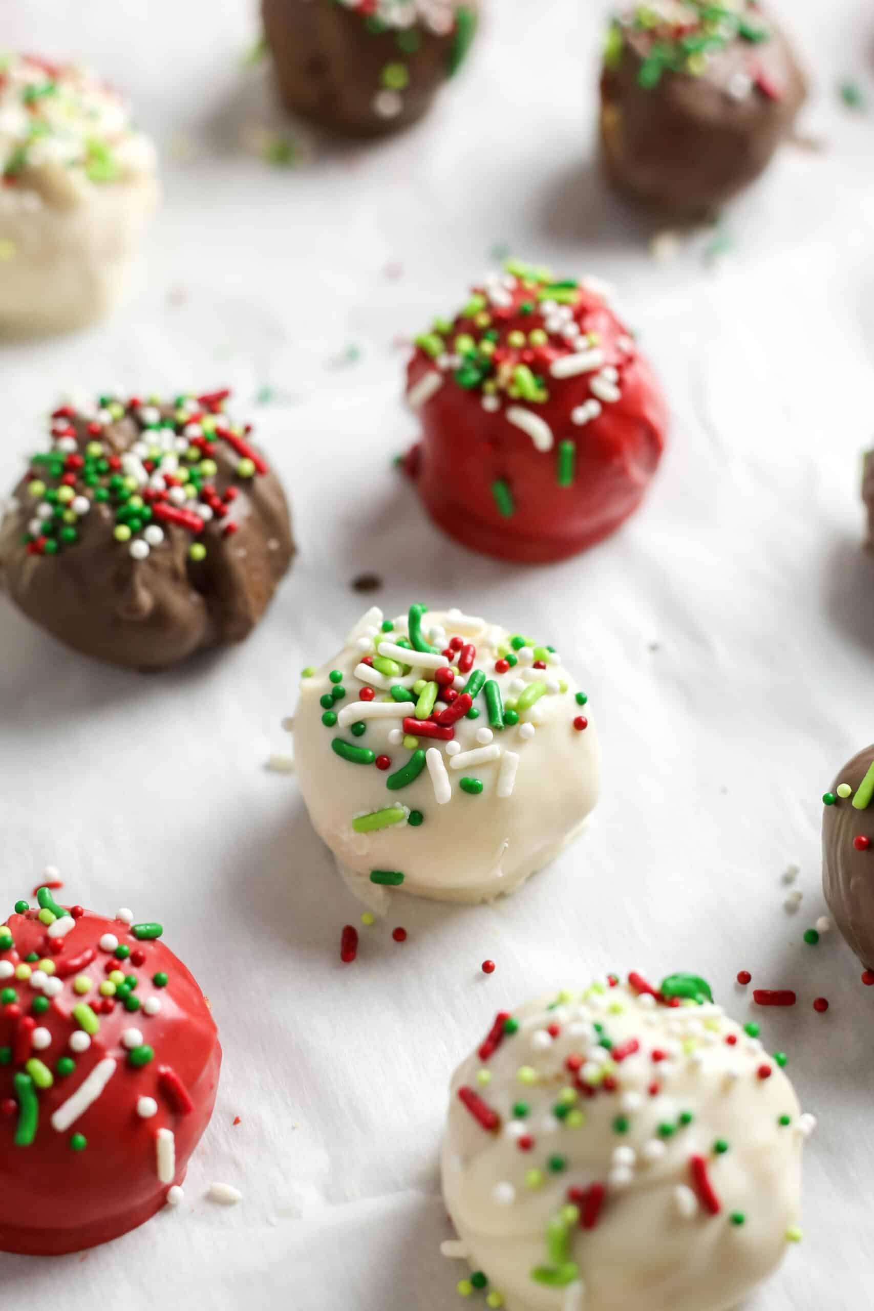 Red, white and brown Christmas cake balls on sheet pan with sprinkles.