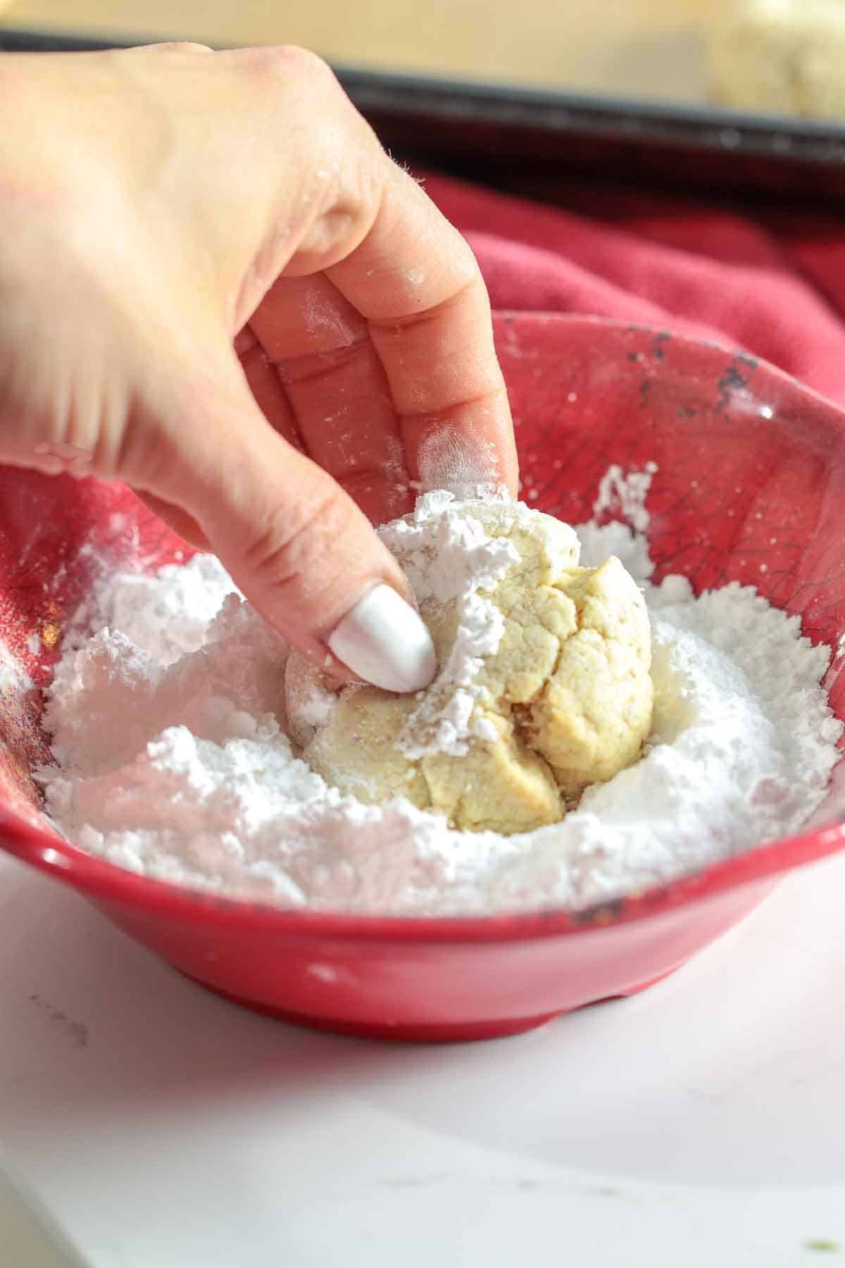 Dipping kourabiedes in confectioners sugar.