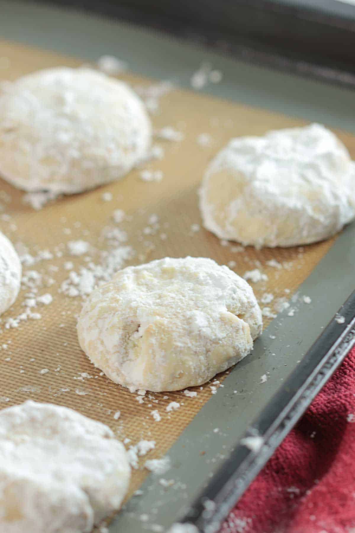 Greek kourabiethes on baking sheet covered in powdered sugar.