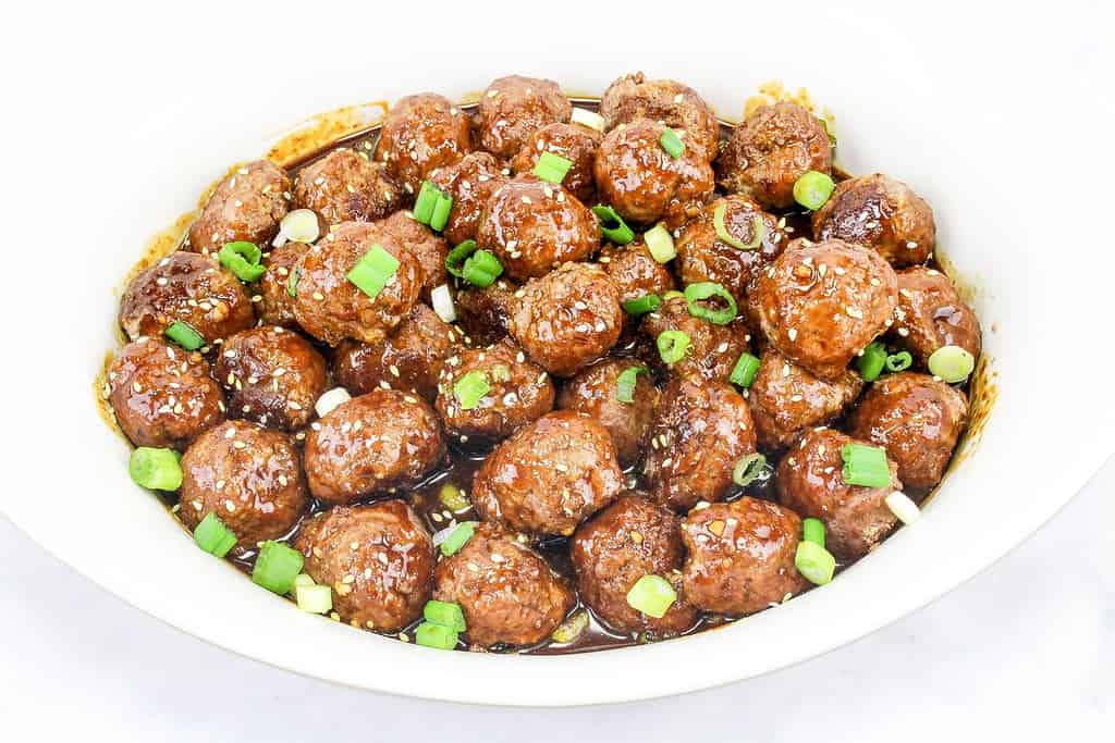 Asian meatbaqlls in a white plate with scallions.