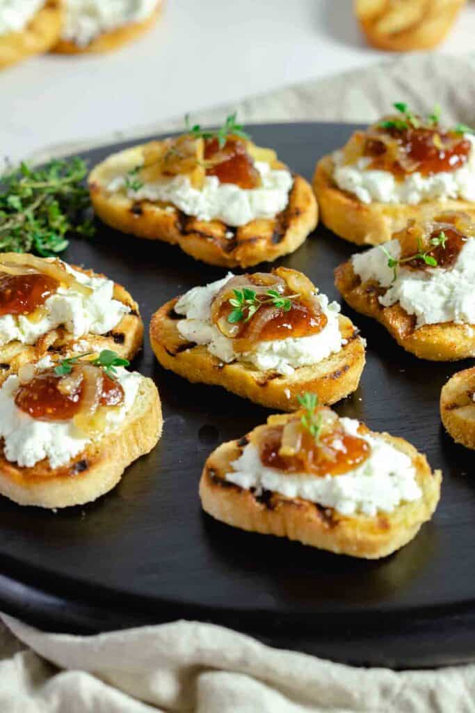Goat cheese and fig jam crostini appetier on cutting board.