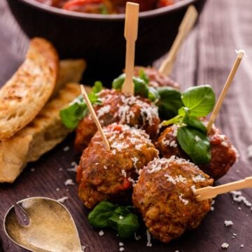 Frozen meatballs appetizer with toothpick skewers and basil on plate.;