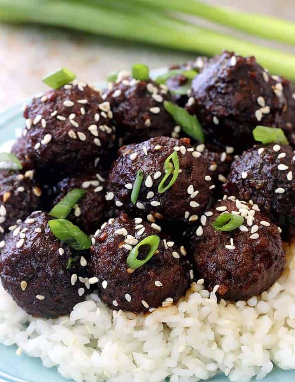 Meatballs on a bed of rice with sesame seeds and green onions as toppings.