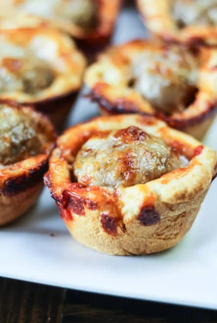 Cheesy meatball bites in a pastry cup on a white plate. 