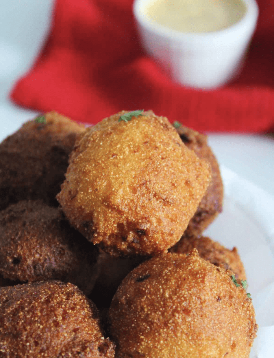 Hush puppies on a plate with a dipping sauce and a red napkin.