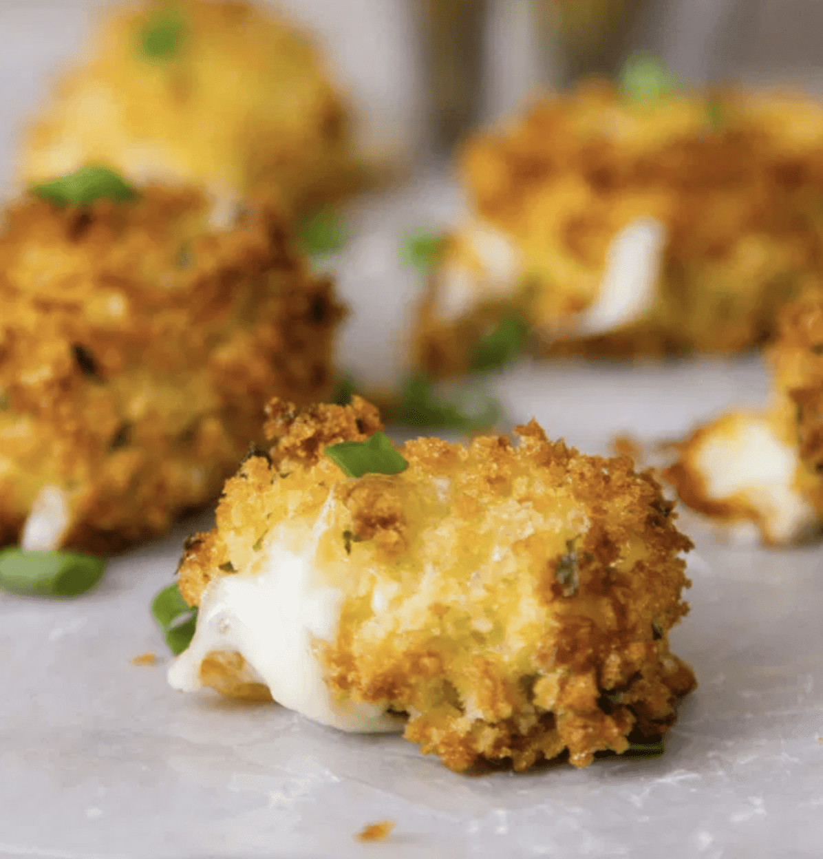 Mozzarella bites with breading on a white serving board.