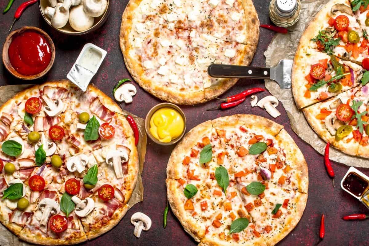 Pizzas on a table with veggies and sauces.