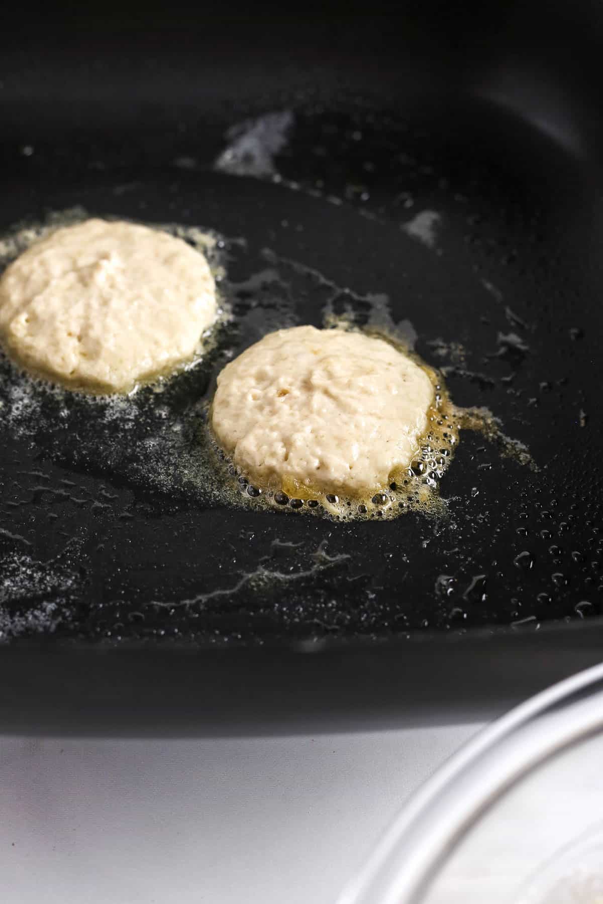 Pancake batter frying on a cast iron skillet.