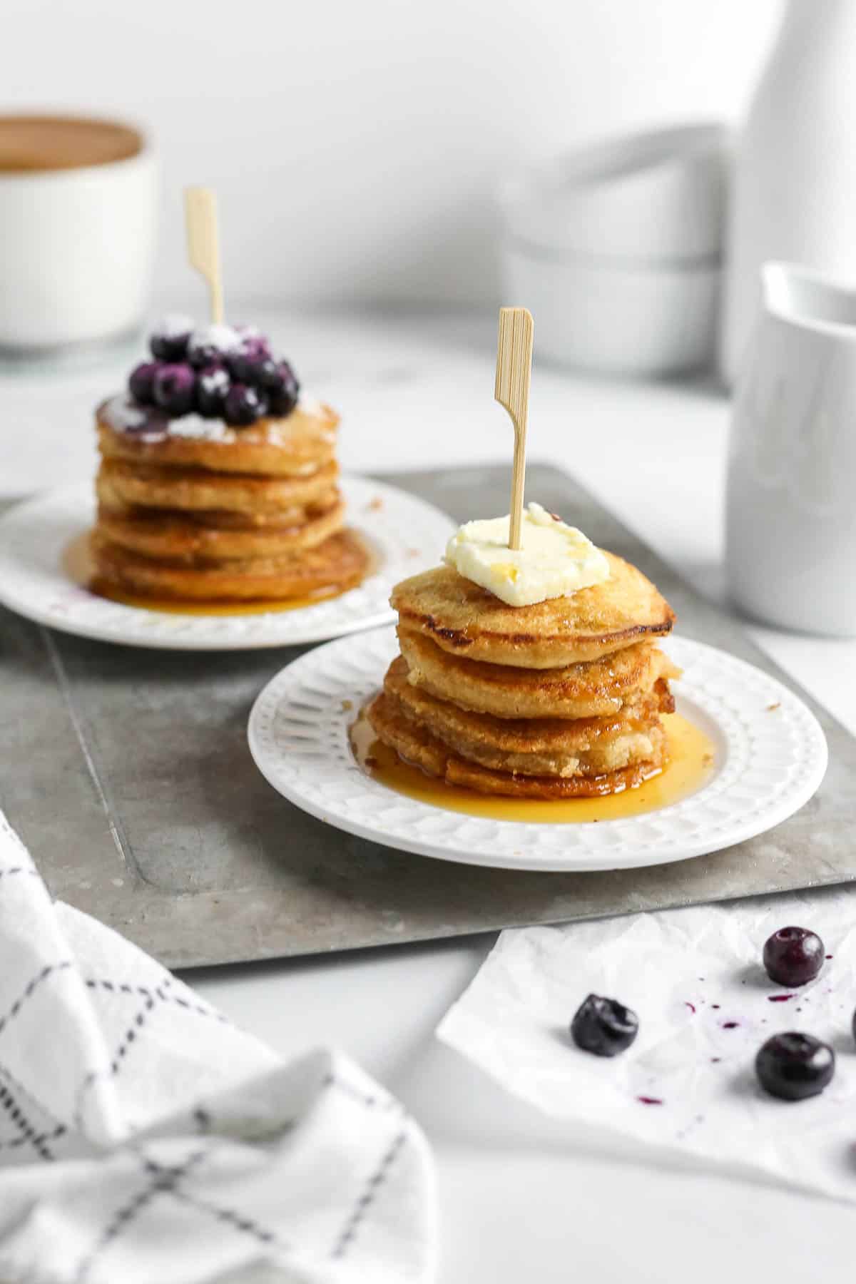 Mini pancake stacks on plates with butter and blueberries on top.