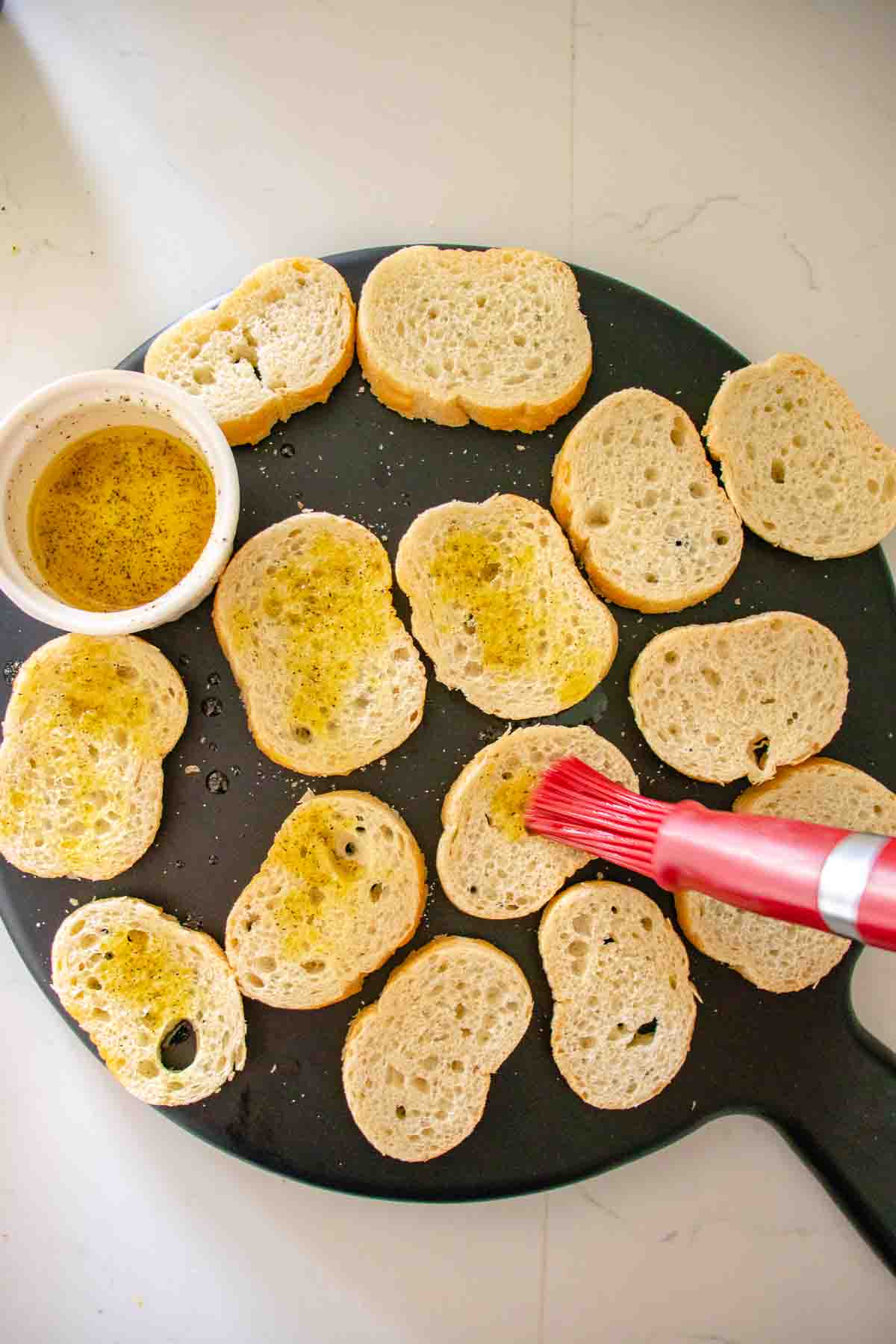 Sliced bread on cutting board being brushed with olive oil.