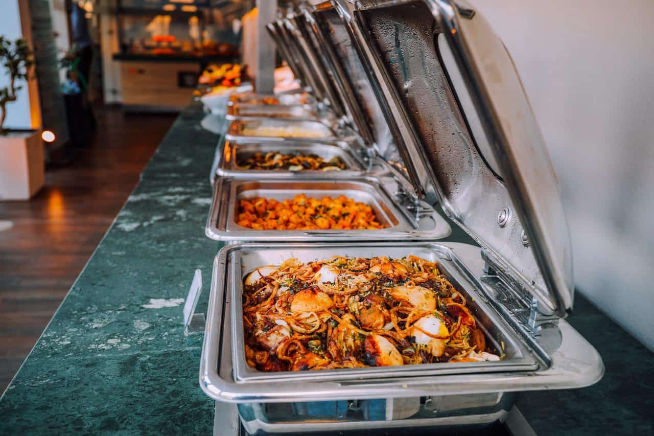 Assorted cooked foods inside food warming dishes for a buffet.