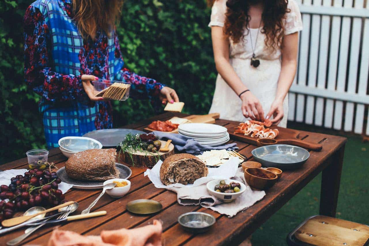 Unrecognizable women serving table with assorted appetizers in garden.