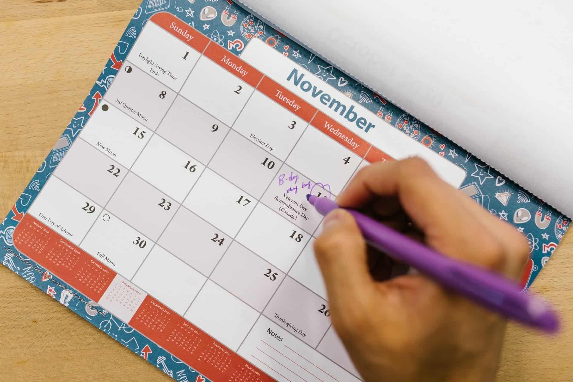 Person Holding Purple Click Pen and Writing on Calendar.