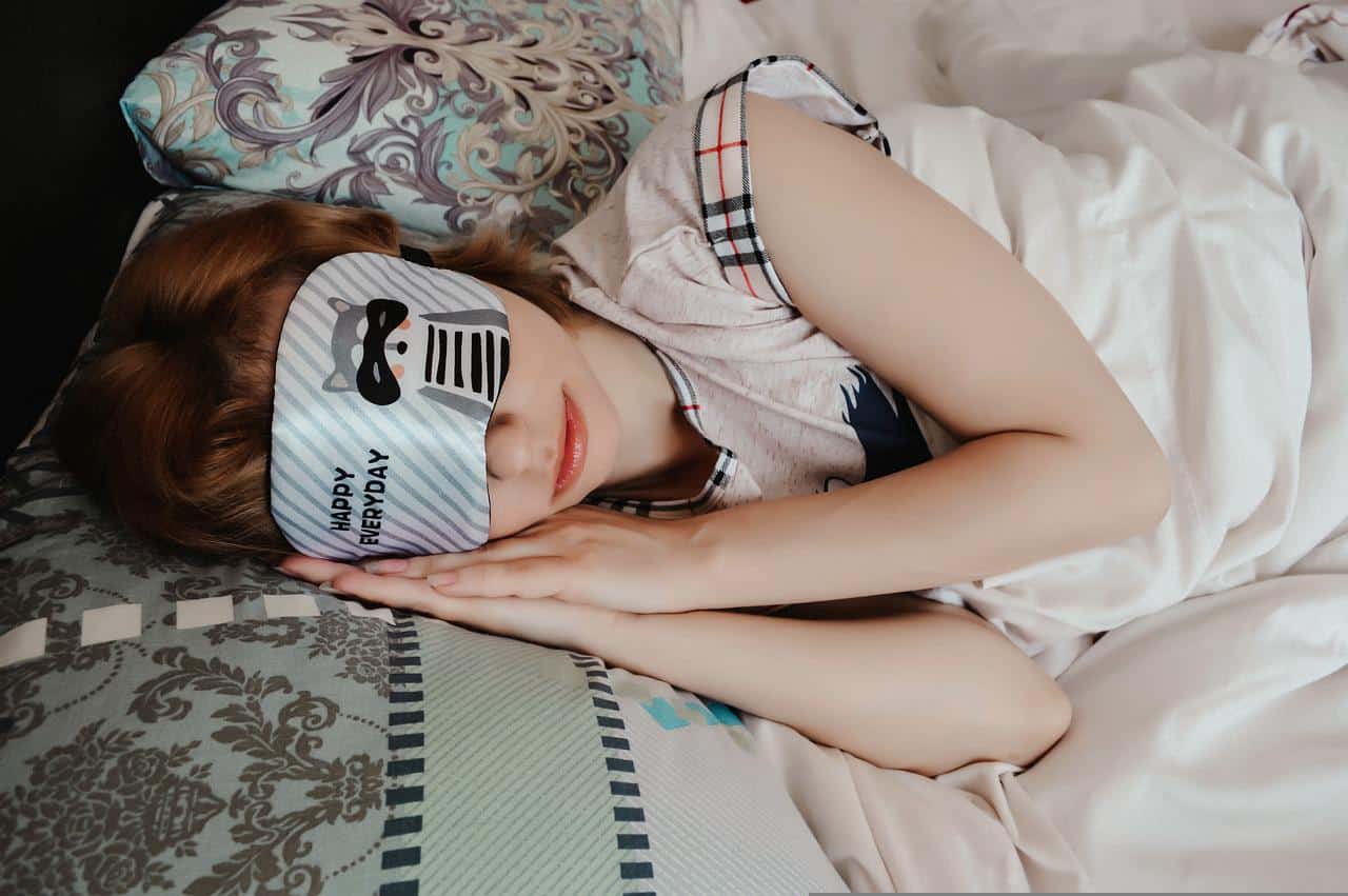 Young girl lying down on bed with sleeping mask.