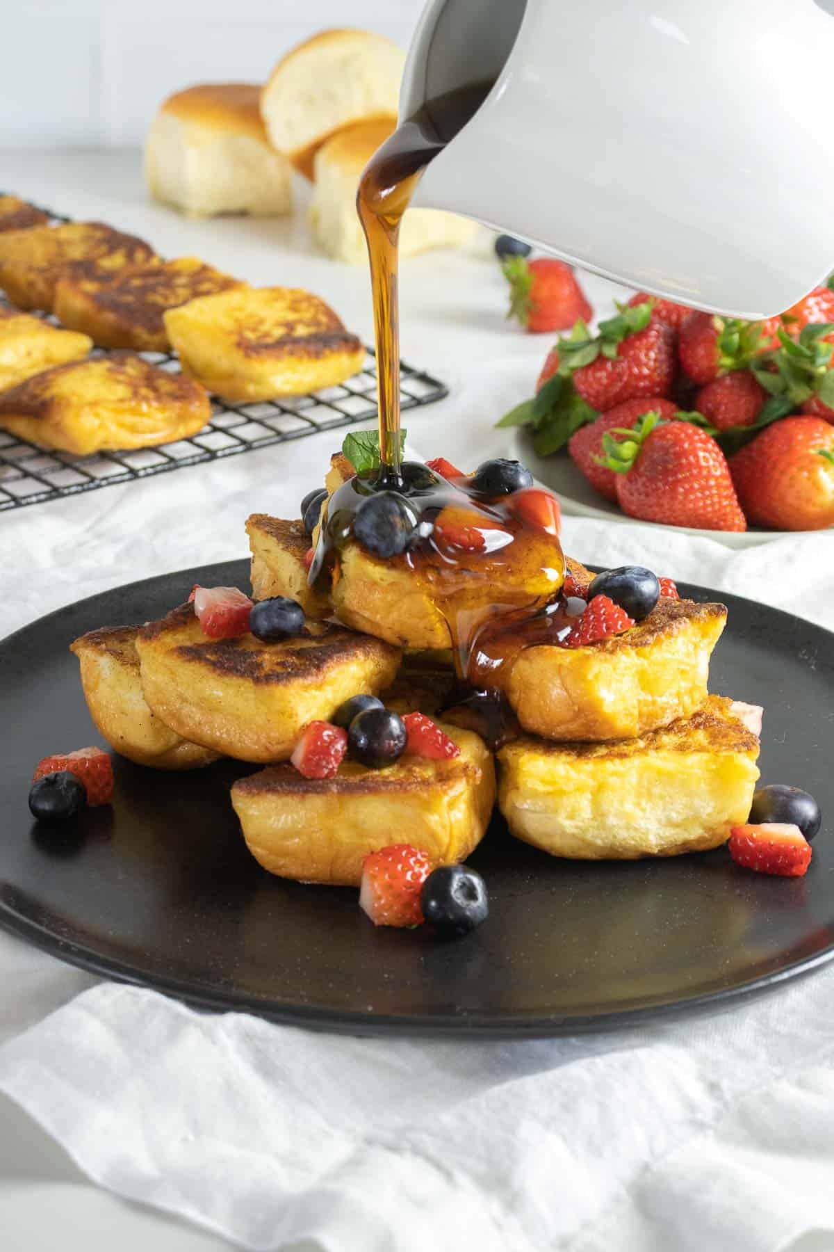 Hawaiian sweet bread French toast on a plate with berries and maple syrup.
